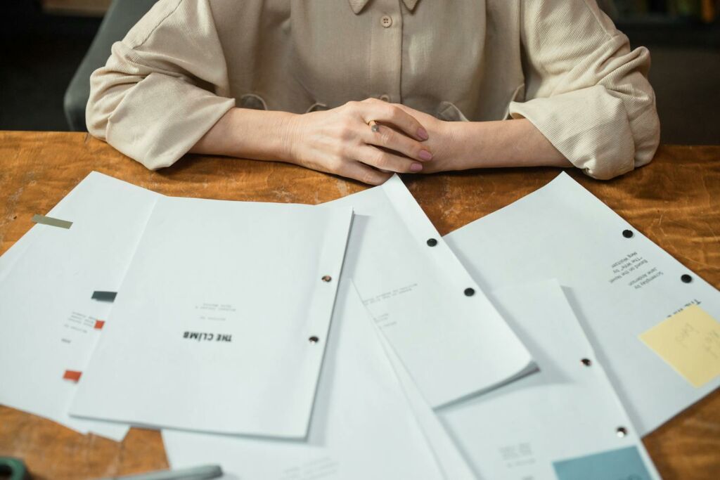 Close-up of a woman's hands with business documents on a wooden desk in an office setting.